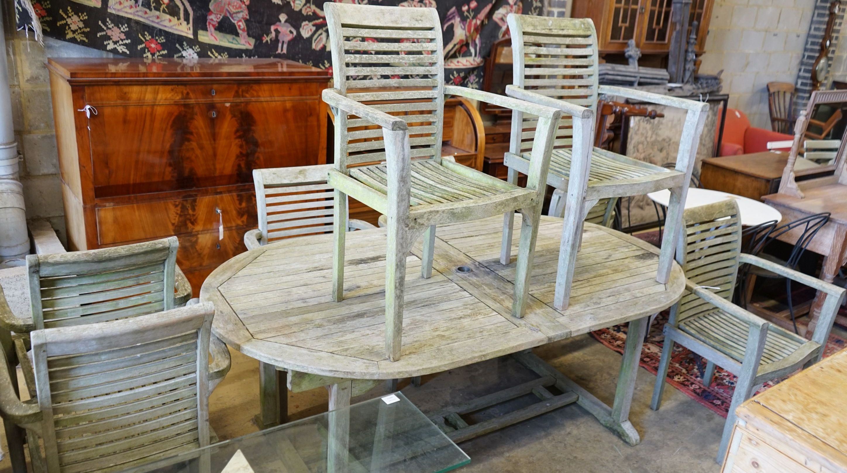 A weathered teak extending oval garden table, length 196cm, width 110cm, height 75cm and eight weathered teak elbow chairs